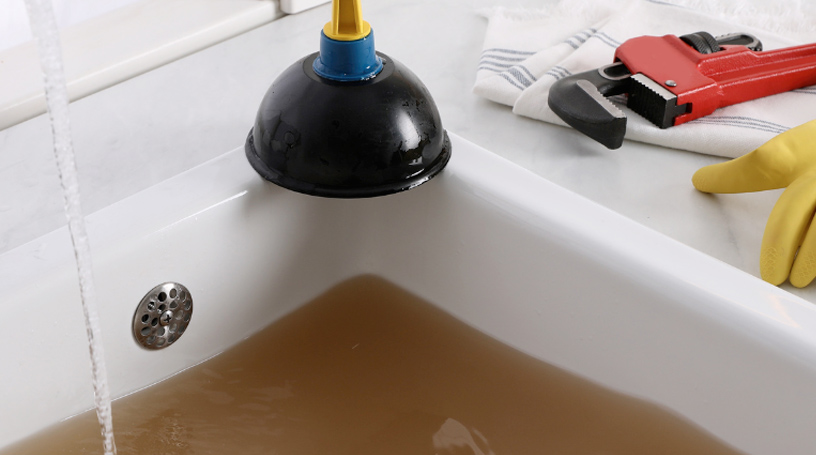 Clogged sink full of dirty water with a wrench and plunger.