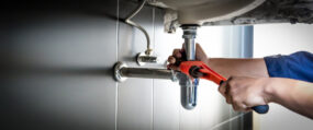 Plumber uses wrench to repair water pipe under sink.