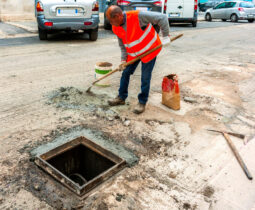 worker prepares the mortar with a fast setting cement to fix the cast-iron manhole cover of an inspection well of the city sewer